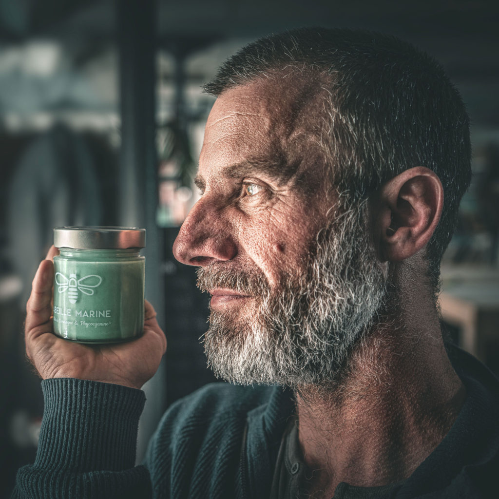 Simon Terrade présentant un pot de miel Abeille Marine à la phycocyanine concentrée, avec des reflets bleus et émeraude.